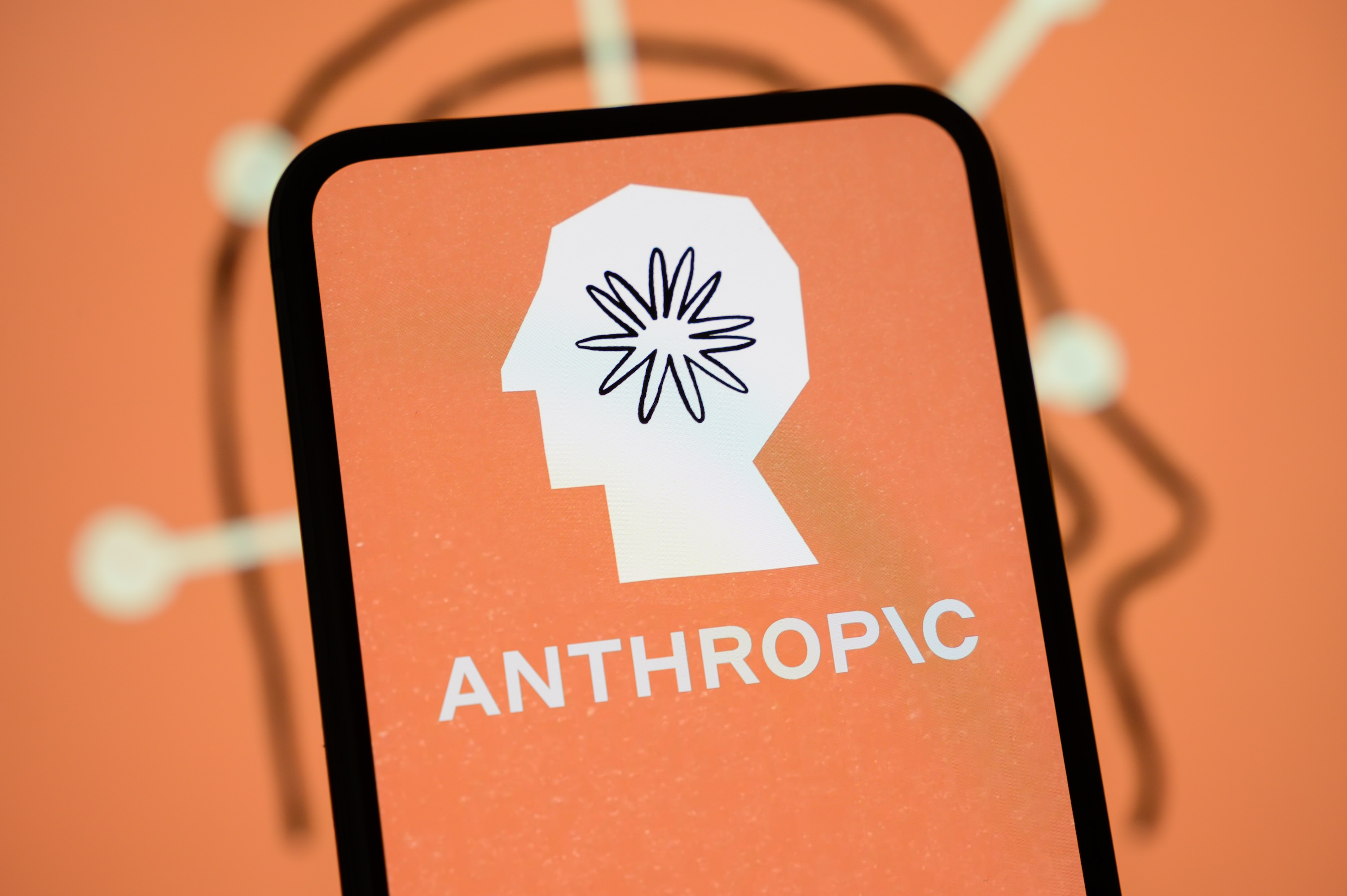 Anthropic-Logo auf einem Smartphone vor KI-Hintergrund. Bildquelle: TechCrunch / Getty Images.